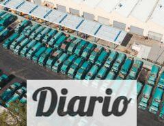 Aerial view of teal trucks lined up in a large industrial parking area next to a warehouse.