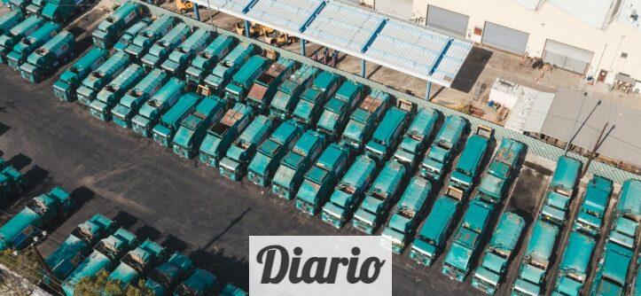 Aerial view of teal trucks lined up in a large industrial parking area next to a warehouse.