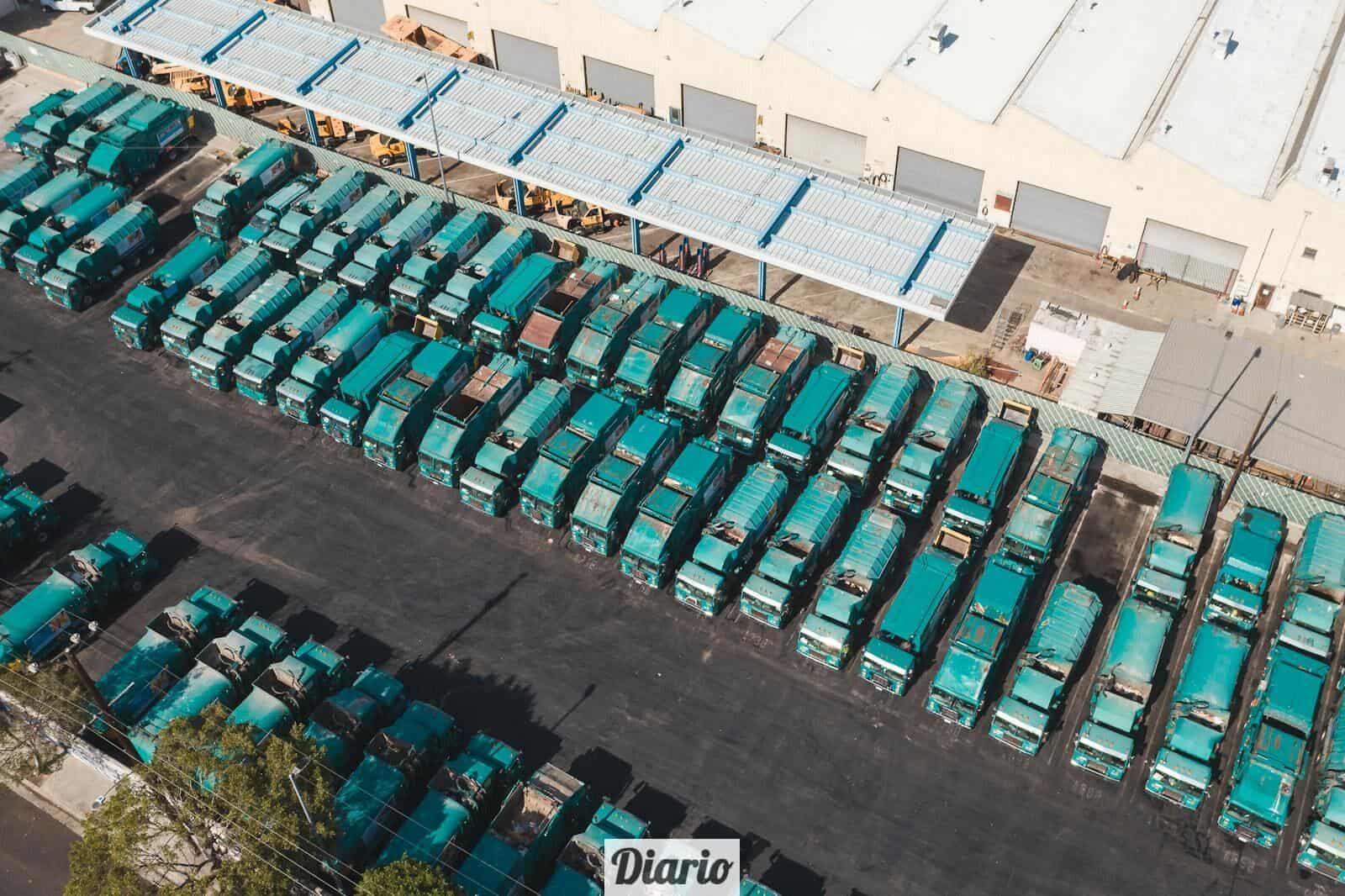Aerial view of teal trucks lined up in a large industrial parking area next to a warehouse.